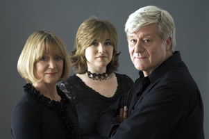 the three performers looking at the camera with a grey background