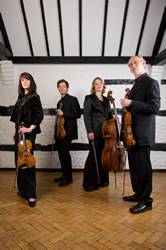 The Fitzwilliam String Quartet standing in a period room holding their instruments
