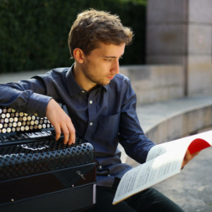 Ben de Souza seated with his accordion looking at some music