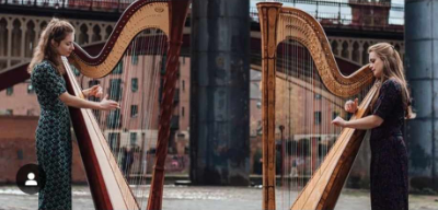 Chroma Harp Duo standing outside with their harps and two bridge structures in the background